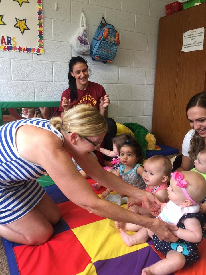 Adults interacting with multiple babies on a colorful mat