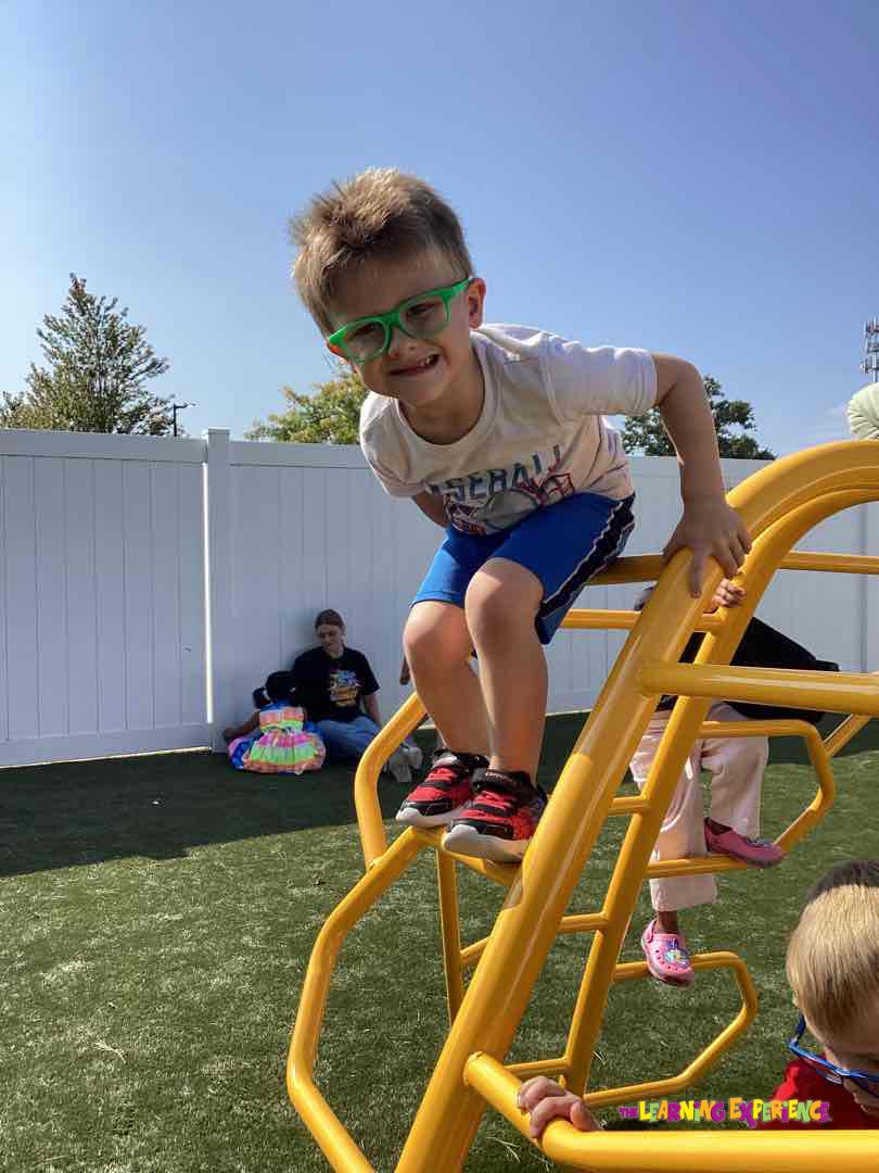 Child in green glasses climbing on yellow playground equipment