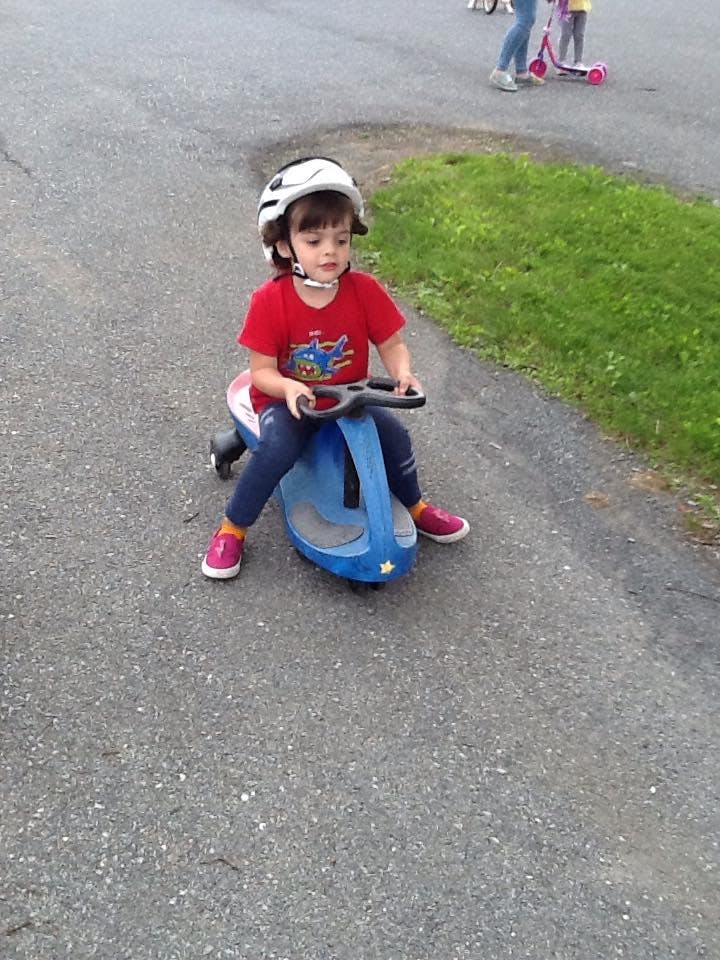 Child wearing a helmet and riding a blue toy car on pavement