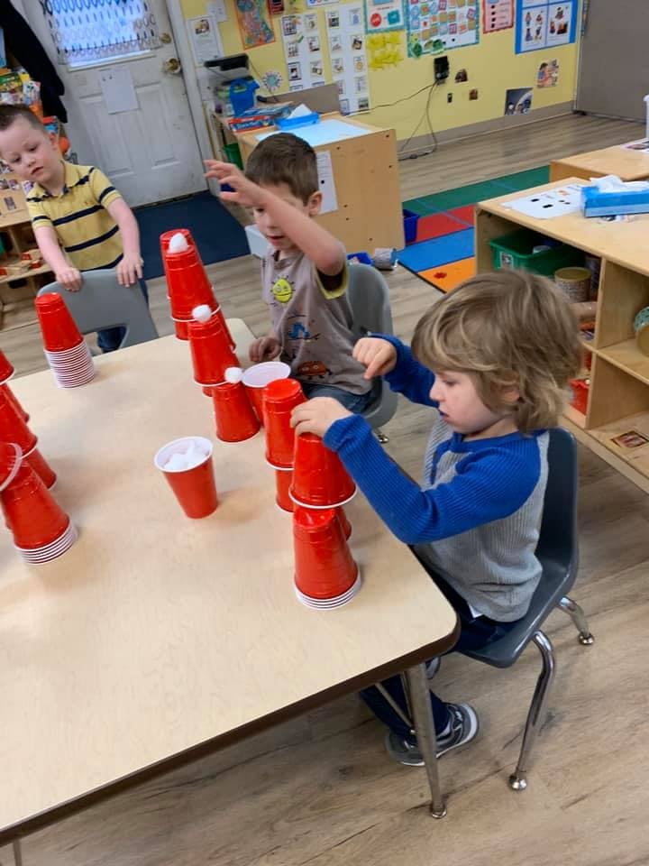 Children stacking red cups at a table in a classroom