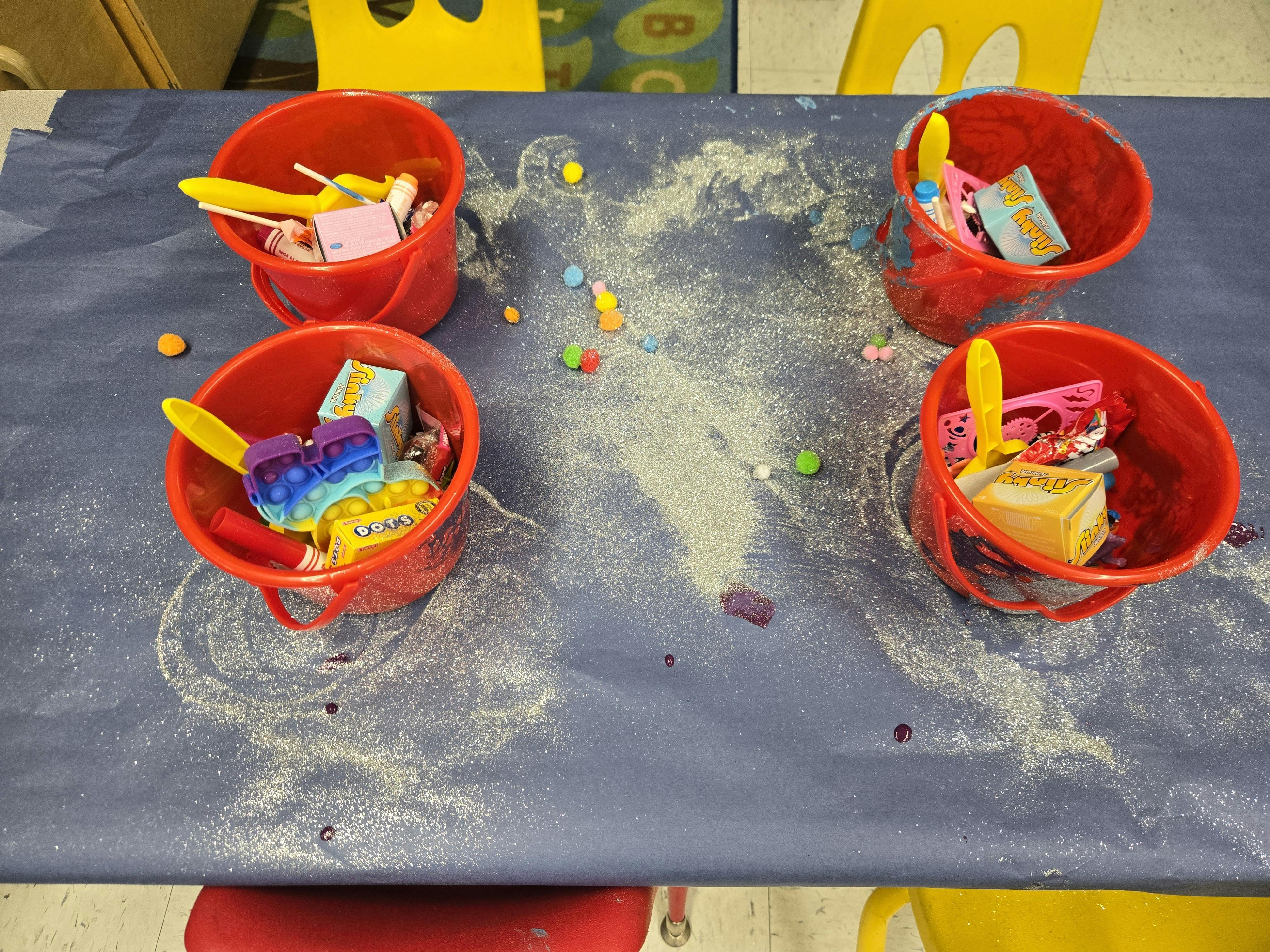 Four red buckets with toys and sand on a blue surface