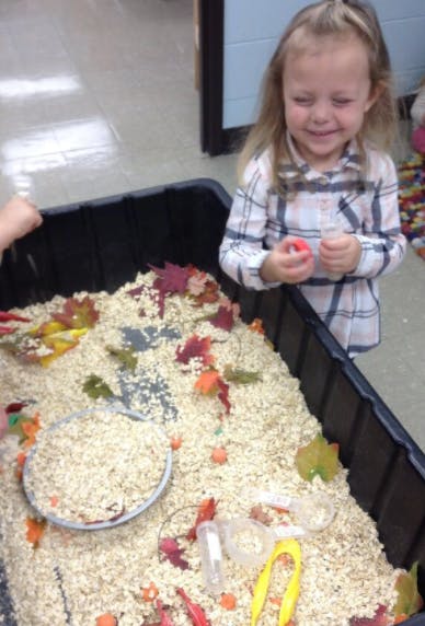 Child playing with a sensory bin filled with rice and autumn leaves