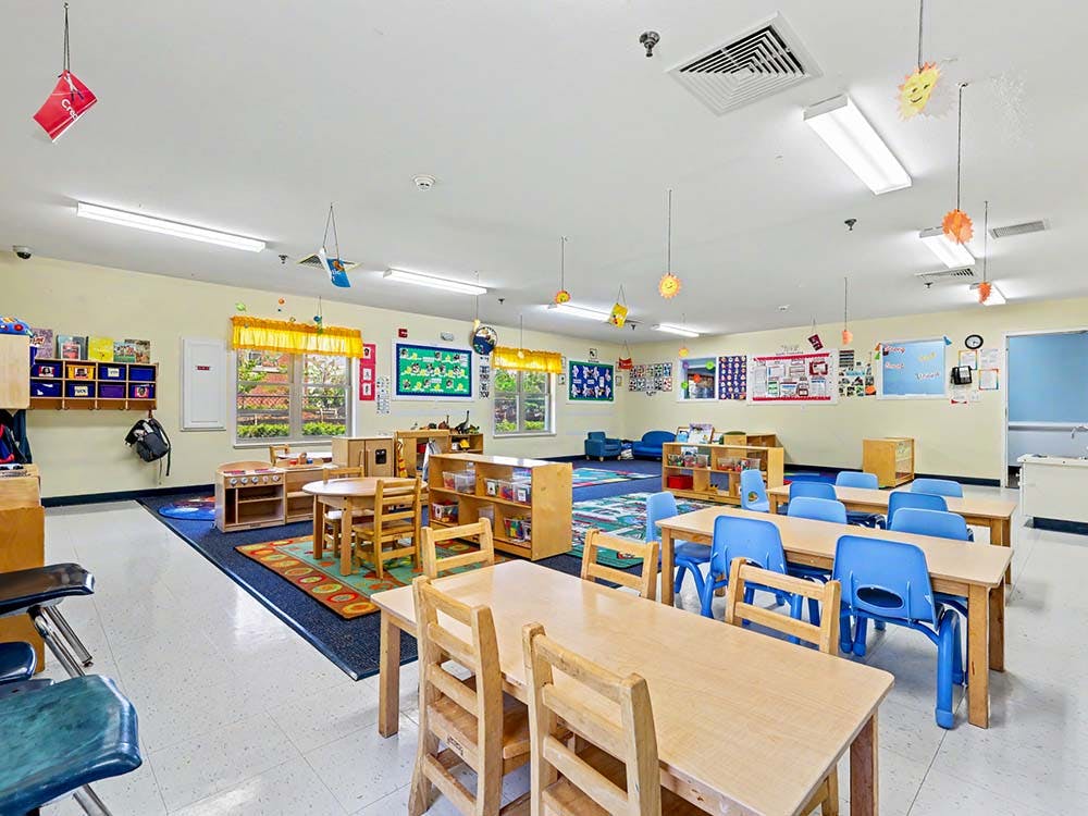 An empty classroom with small wooden tables and blue chairs