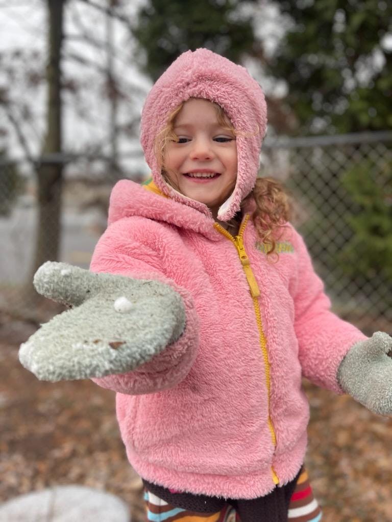 Child in pink coat and mittens holding snow