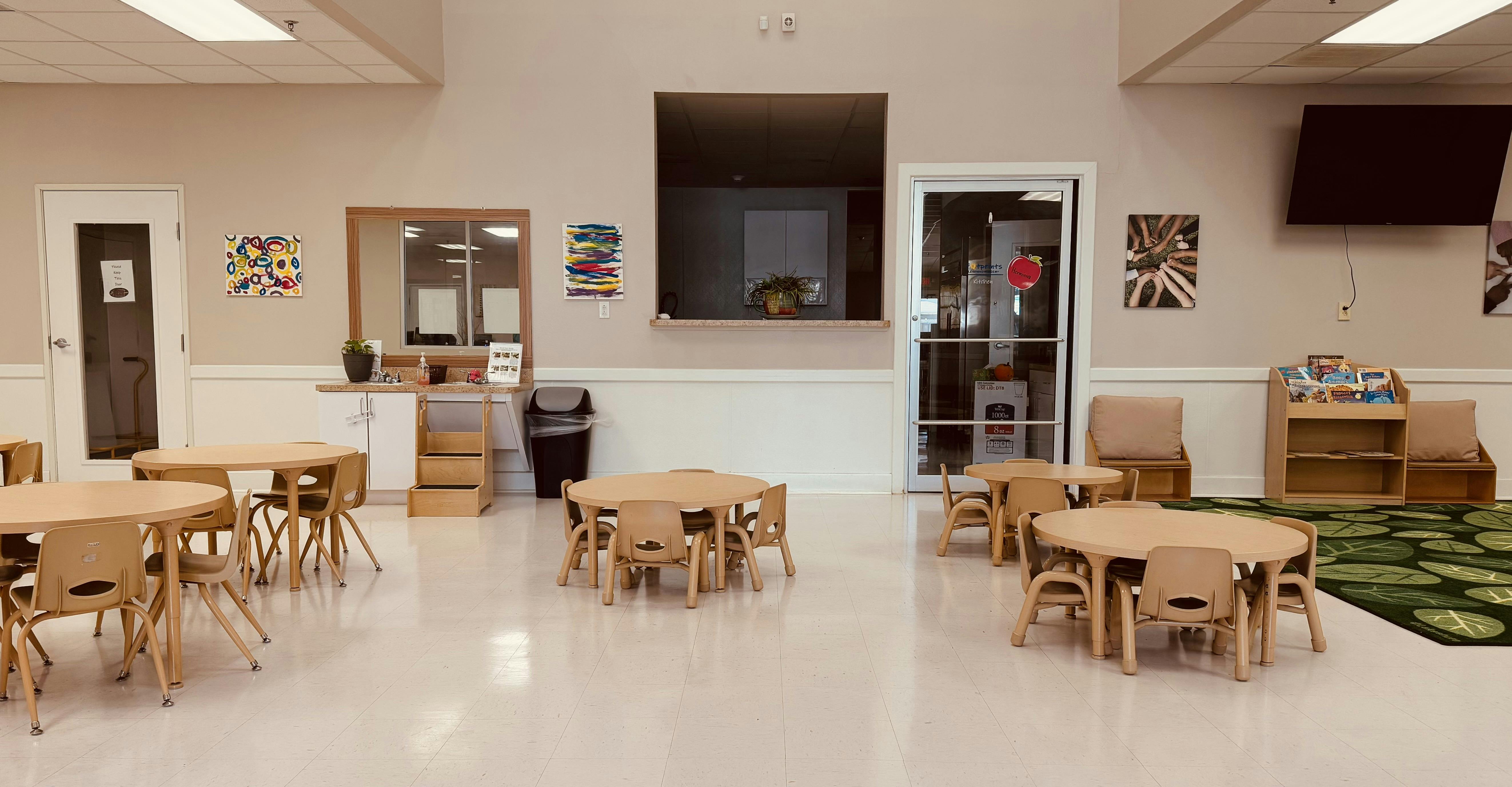 Children's classroom with small tables and chairs, a sink area, and a book display