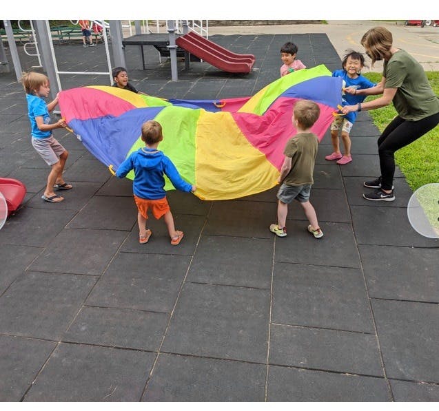 Adult and children playing with a colorful parachute on a playground