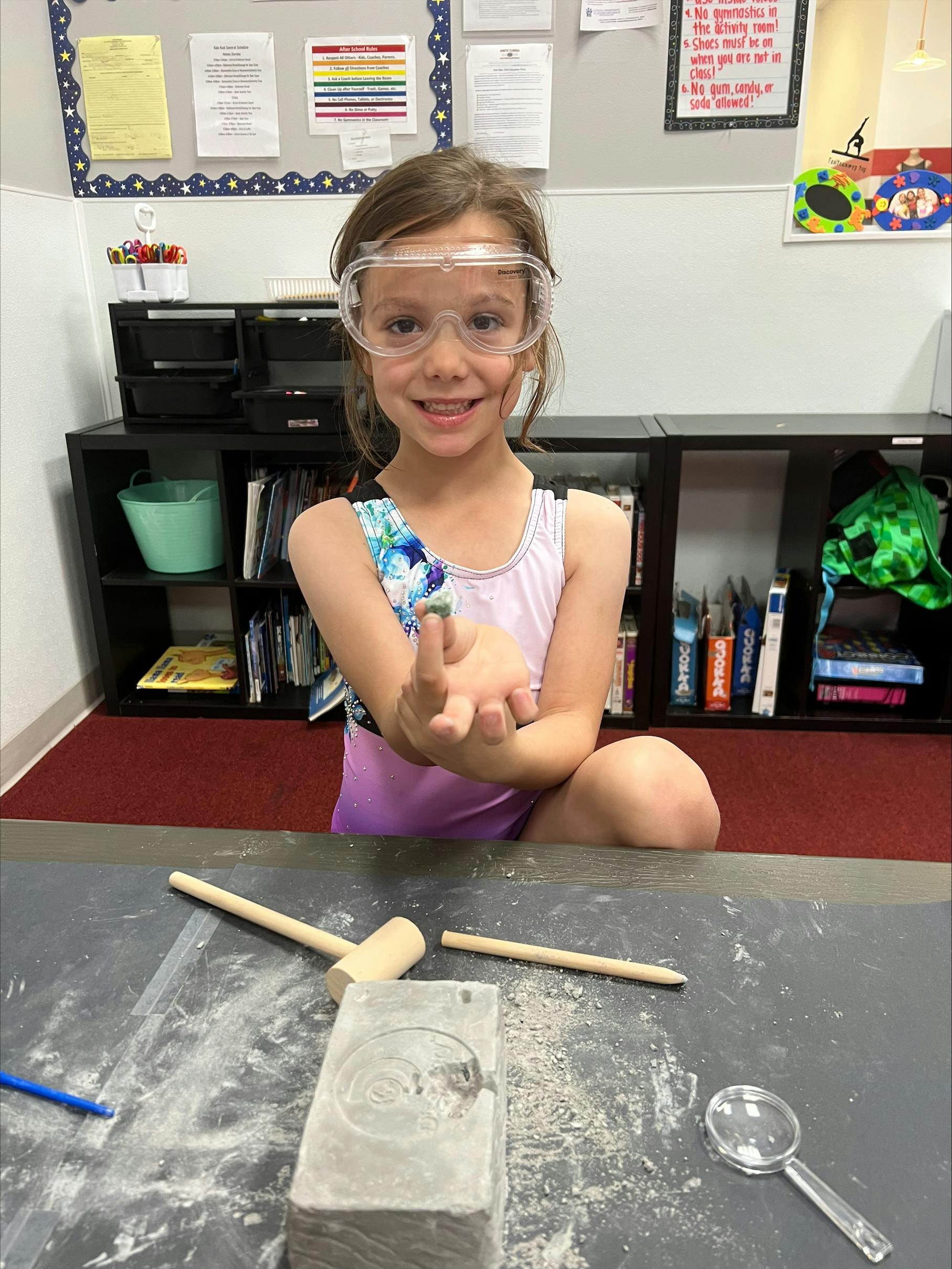 Child wearing safety goggles, holding out hand over a table with tools
