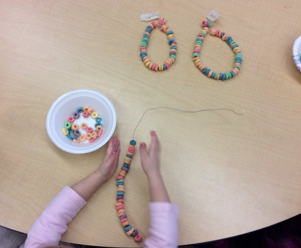 Child's hands stringing colorful cereal pieces onto a string