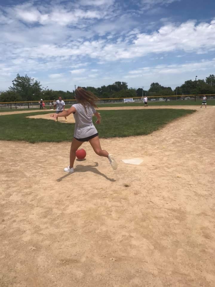 Person kicking a red ball on a baseball field