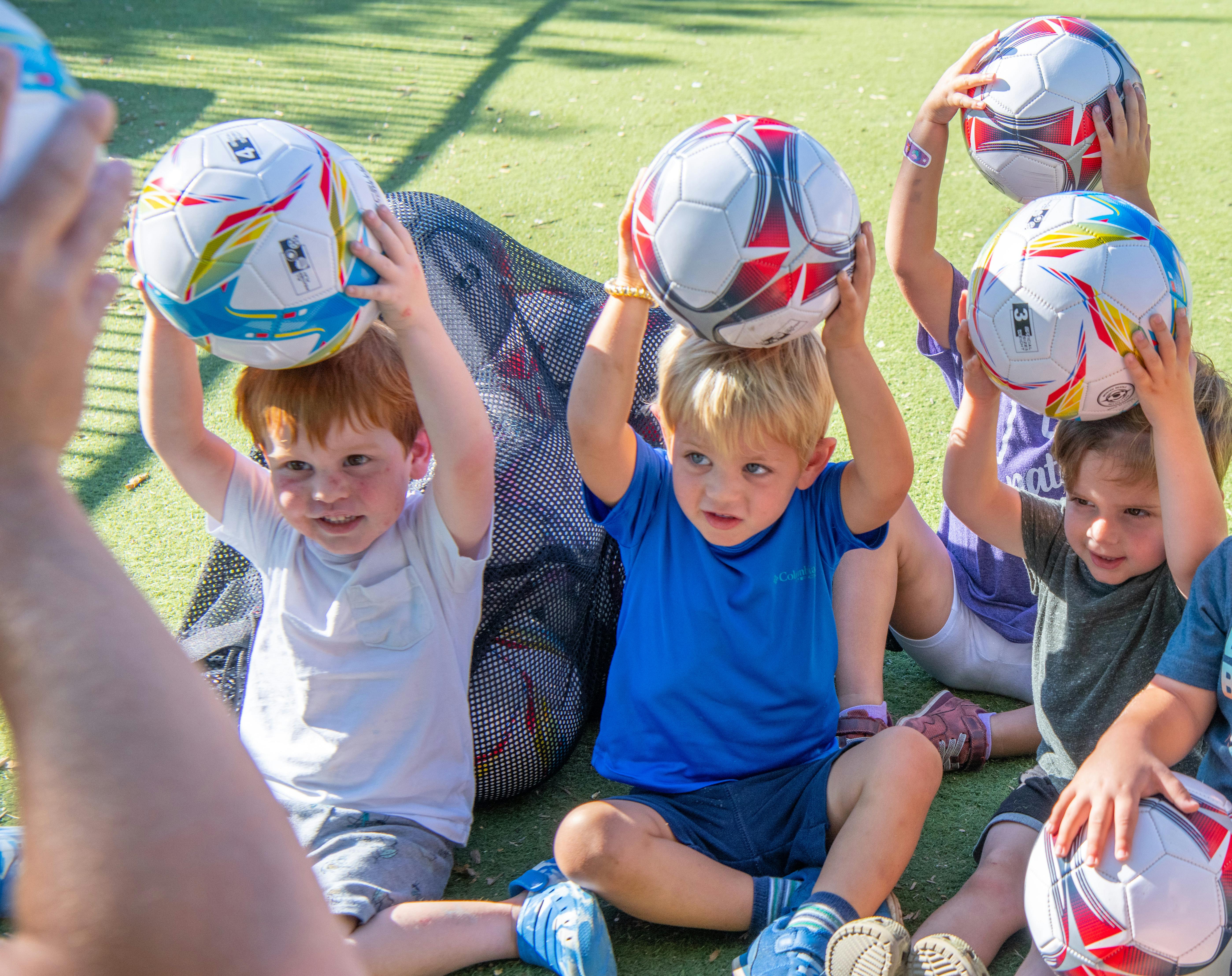 Children holding soccer balls above their heads