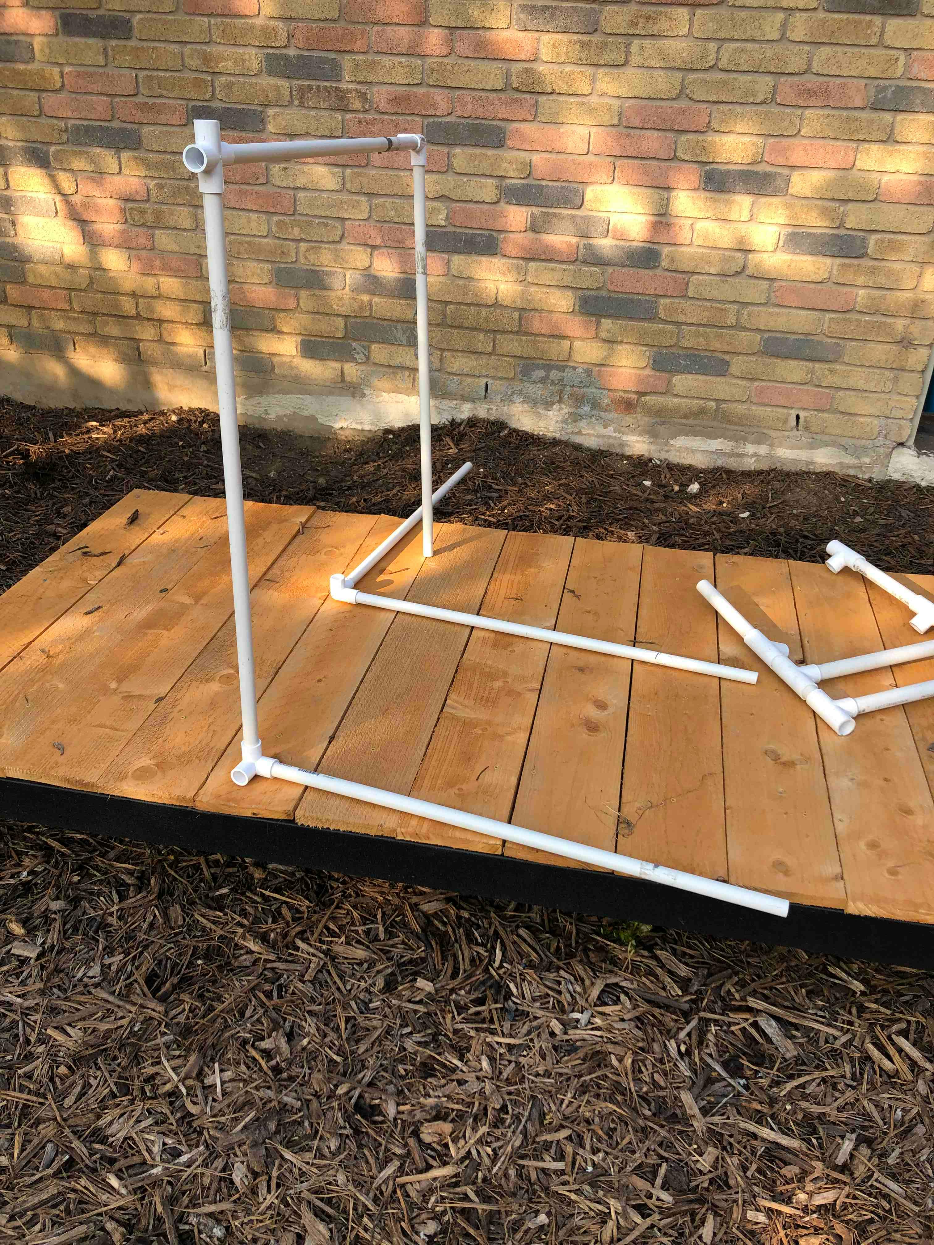 PVC pipe frame partially assembled on a wooden platform
