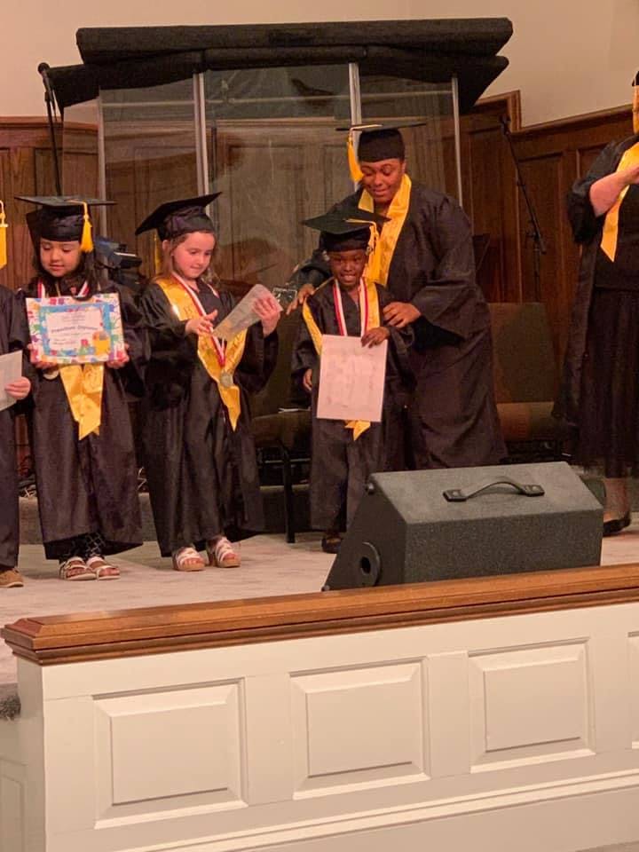 Adult and children in graduation caps and gowns on a stage