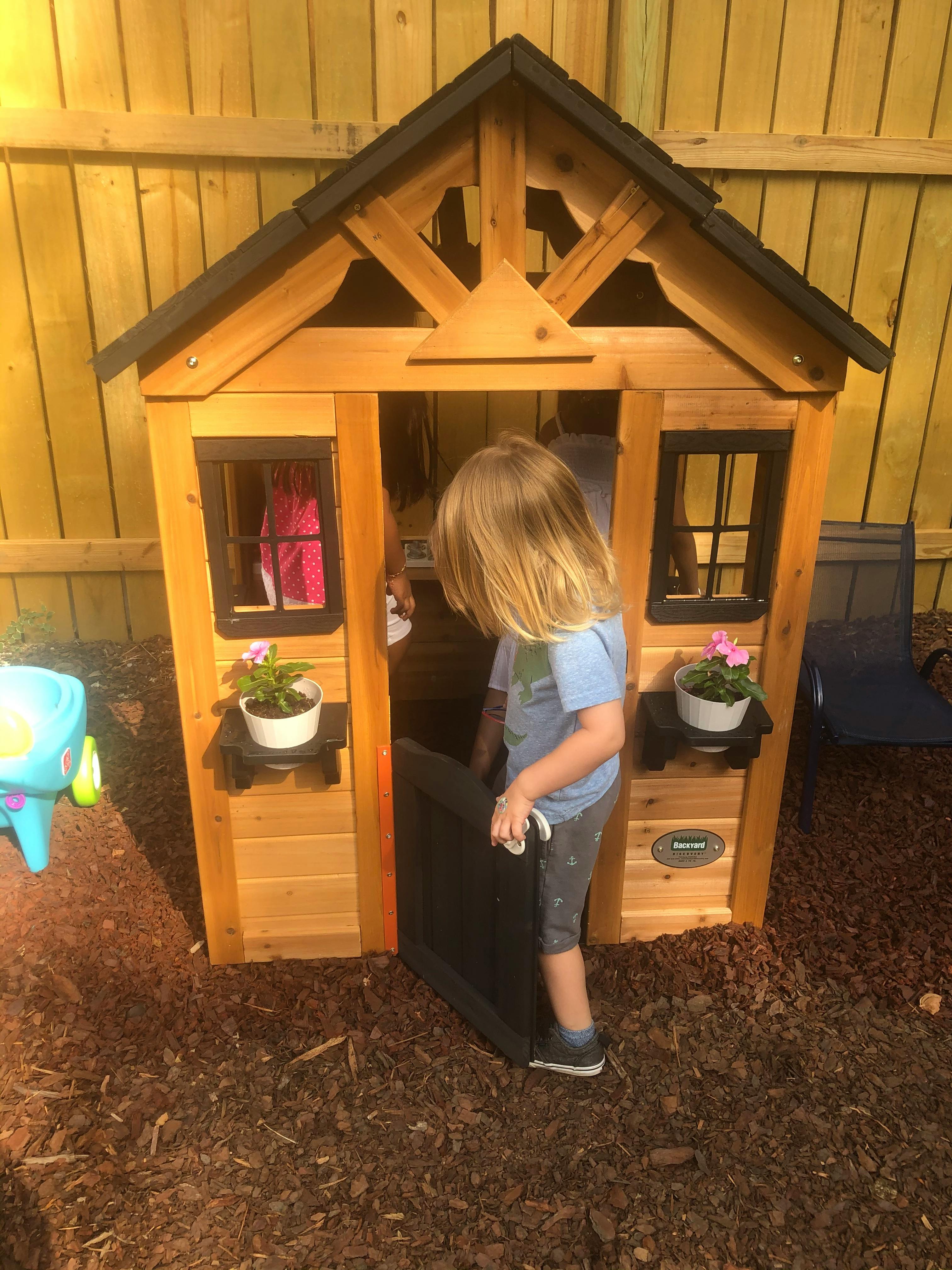 Child standing in the doorway of a wooden playhouse