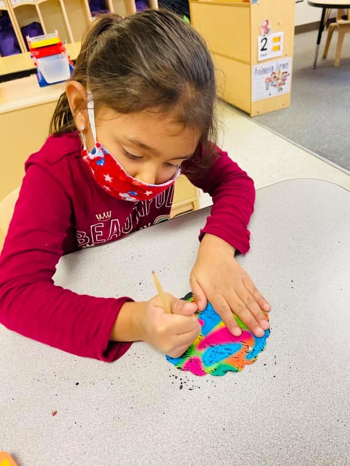 Child in a mask working on a colorful craft at a table