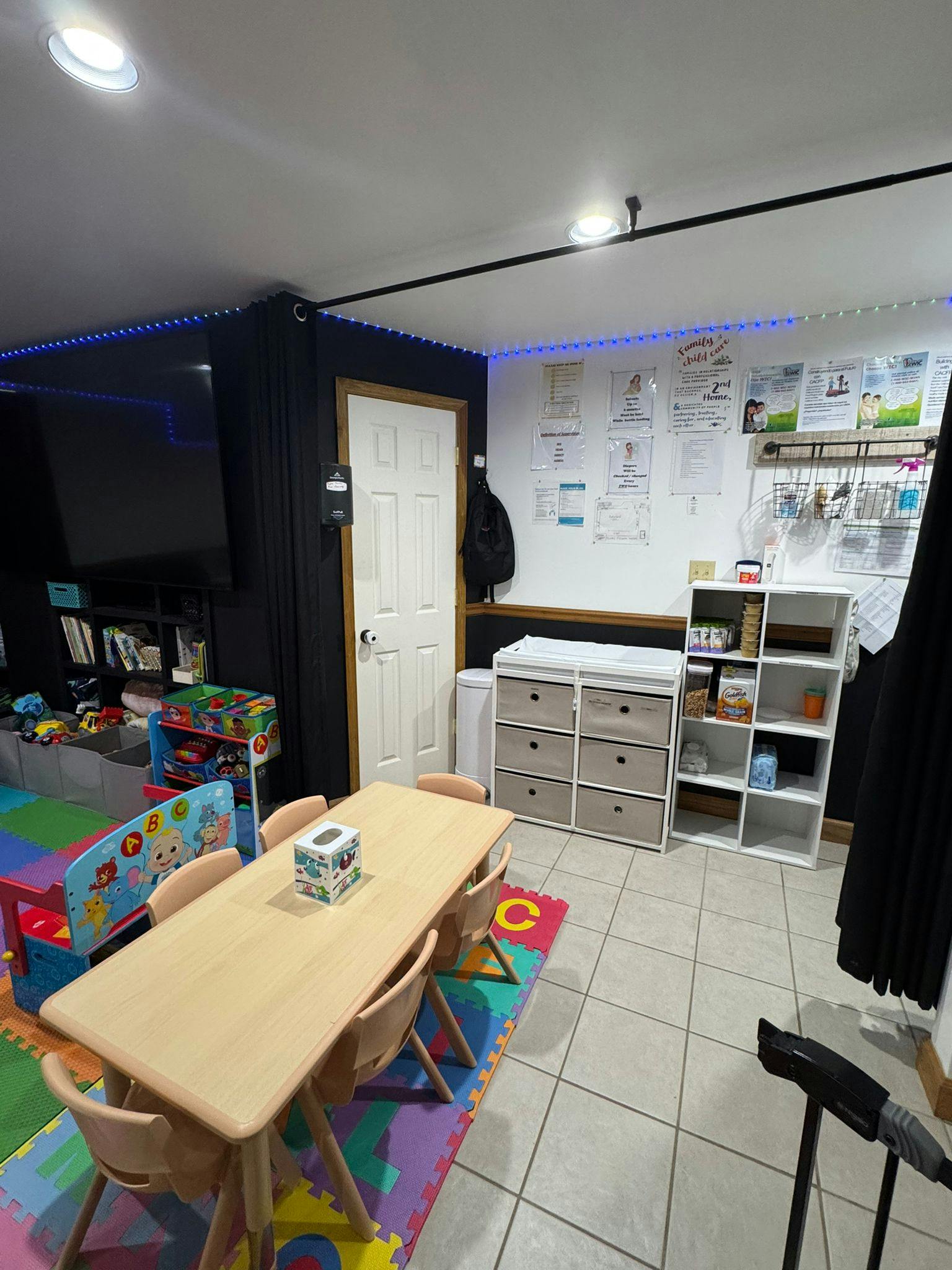 Children's play area with a long table and chairs, storage units, and a TV