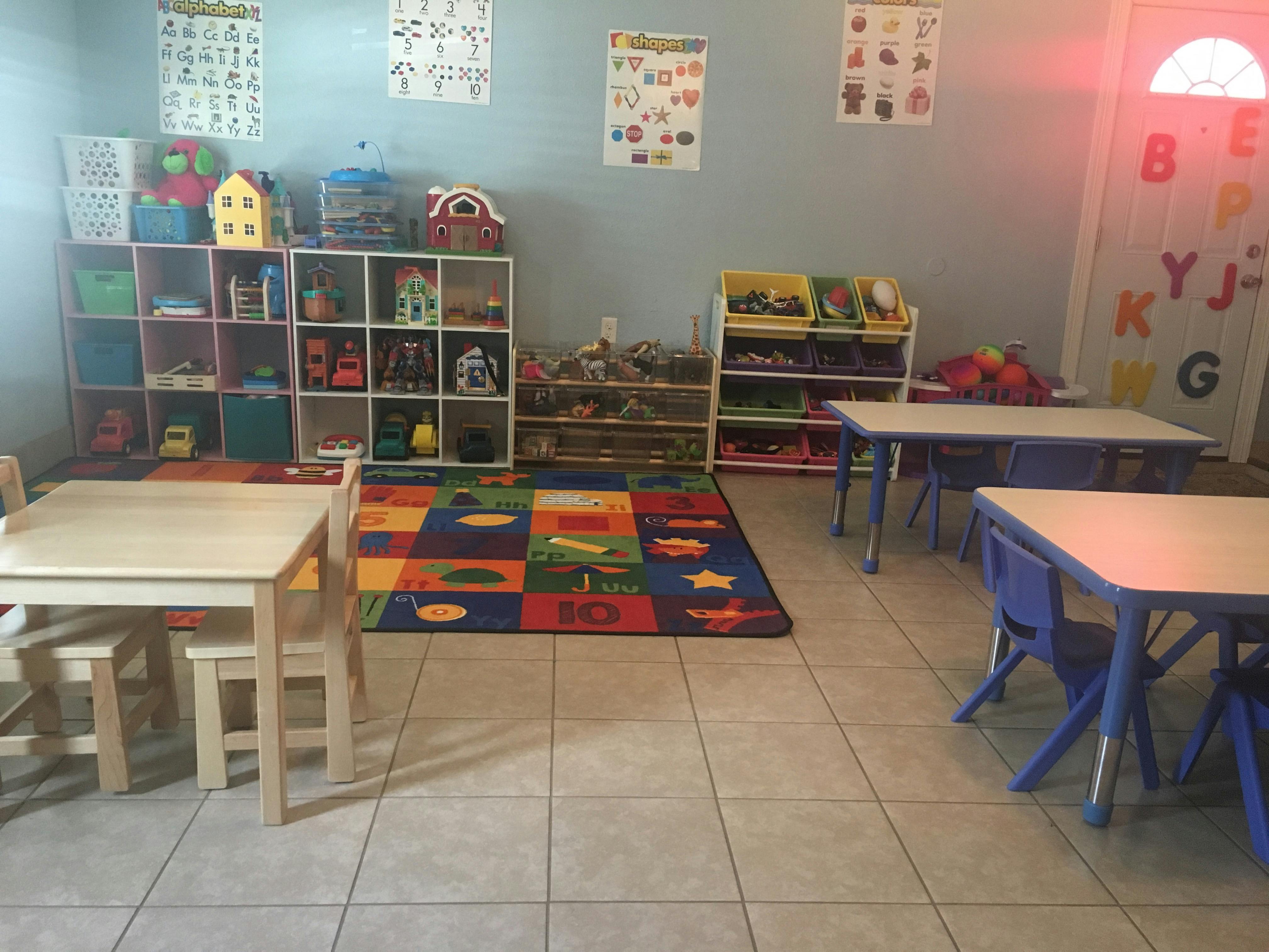 classroom with small tables and chairs, shelves with toys, and a colorful rug
