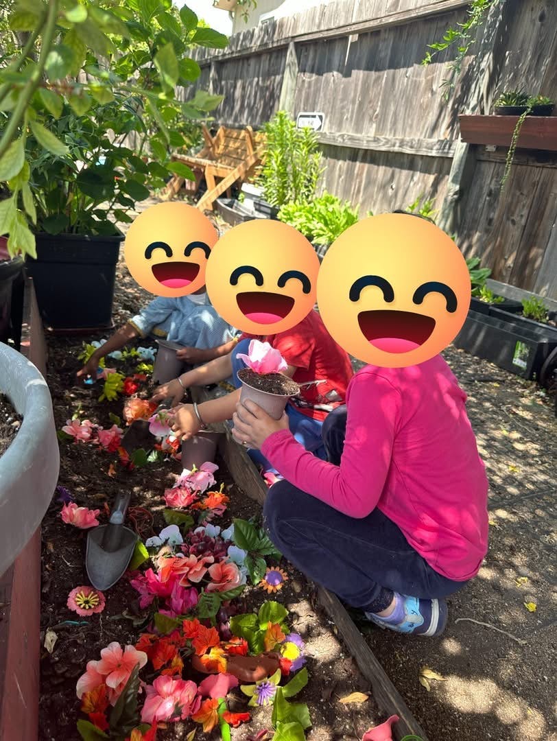Three children planting flowers in a garden bed