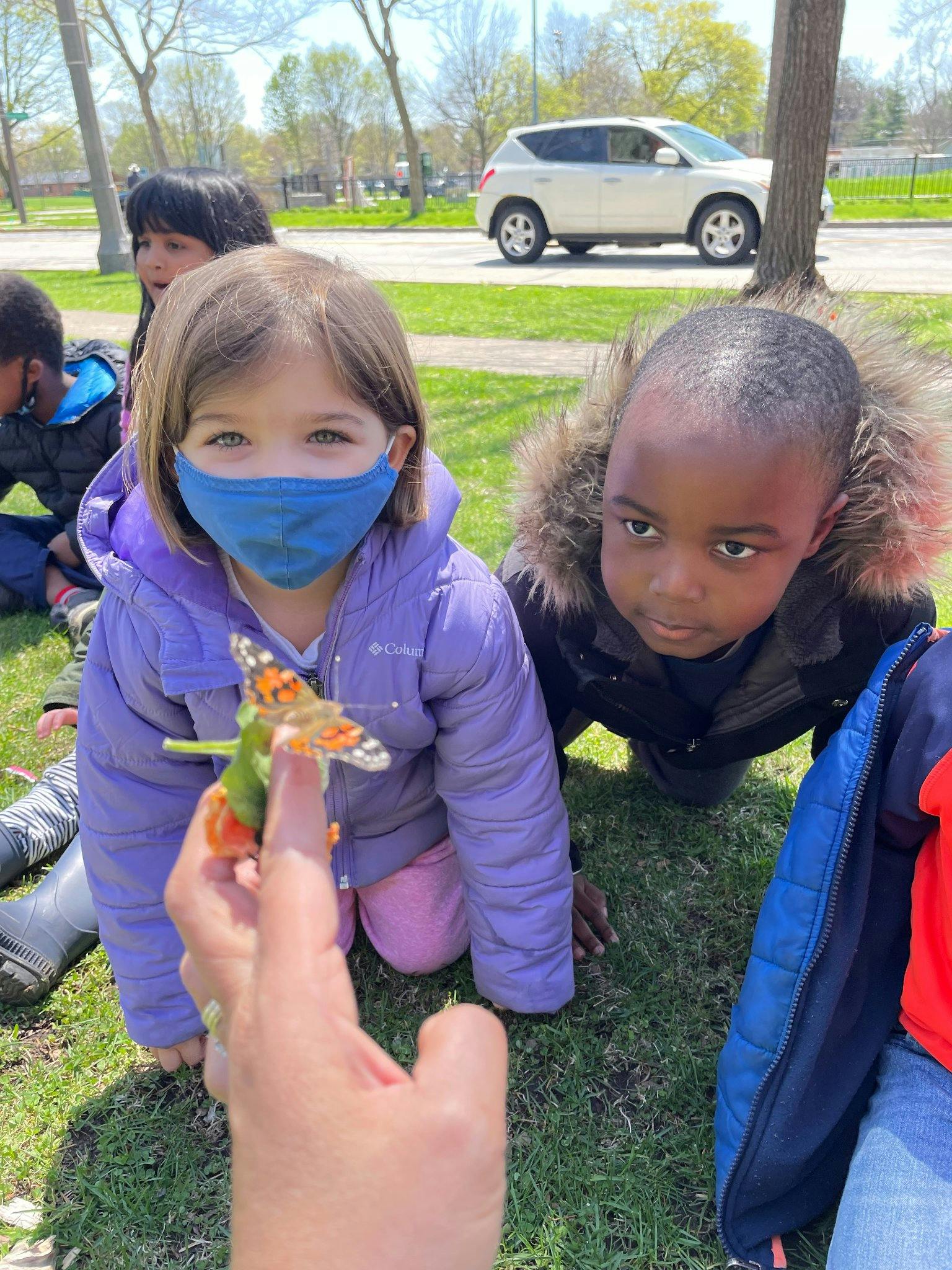 Children on grass looking at a butterfly on a person's finger