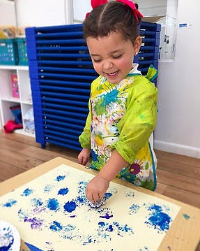 Child in smock painting with blue paint on paper