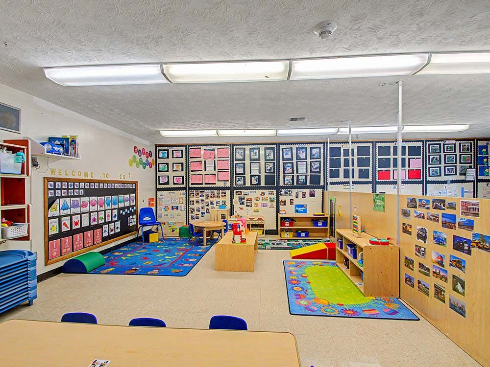 Empty children's classroom with colorful rugs, tables, and learning displays