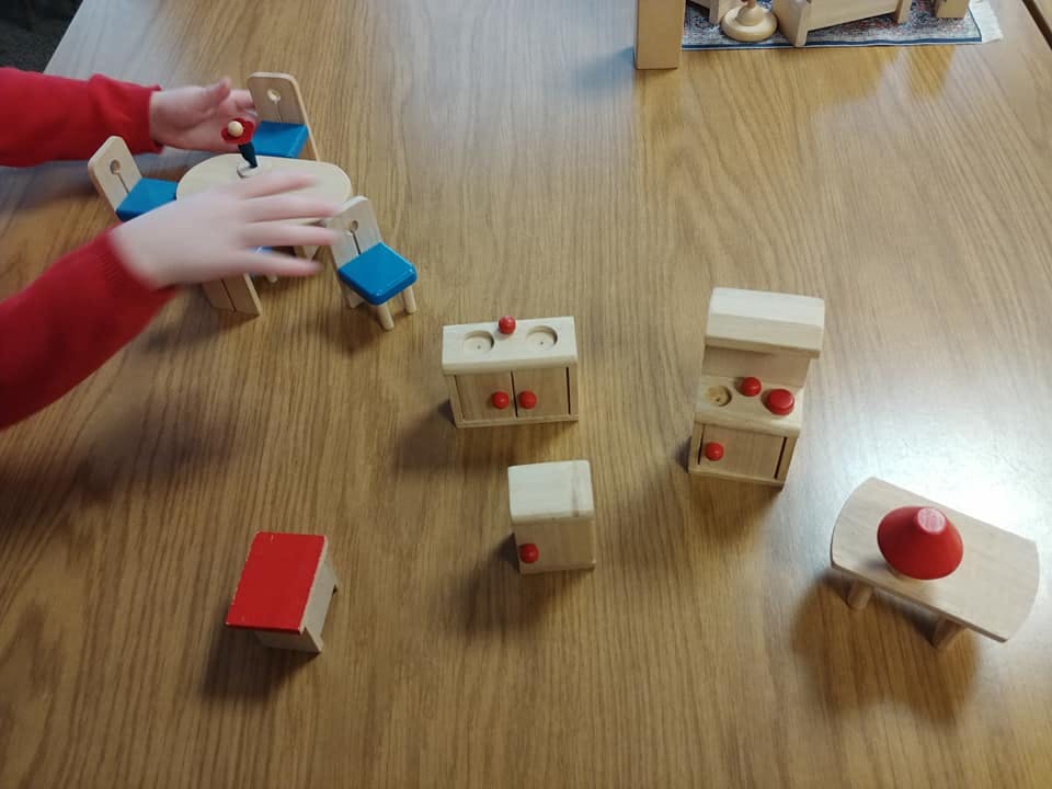Child playing with wooden dollhouse furniture on a table