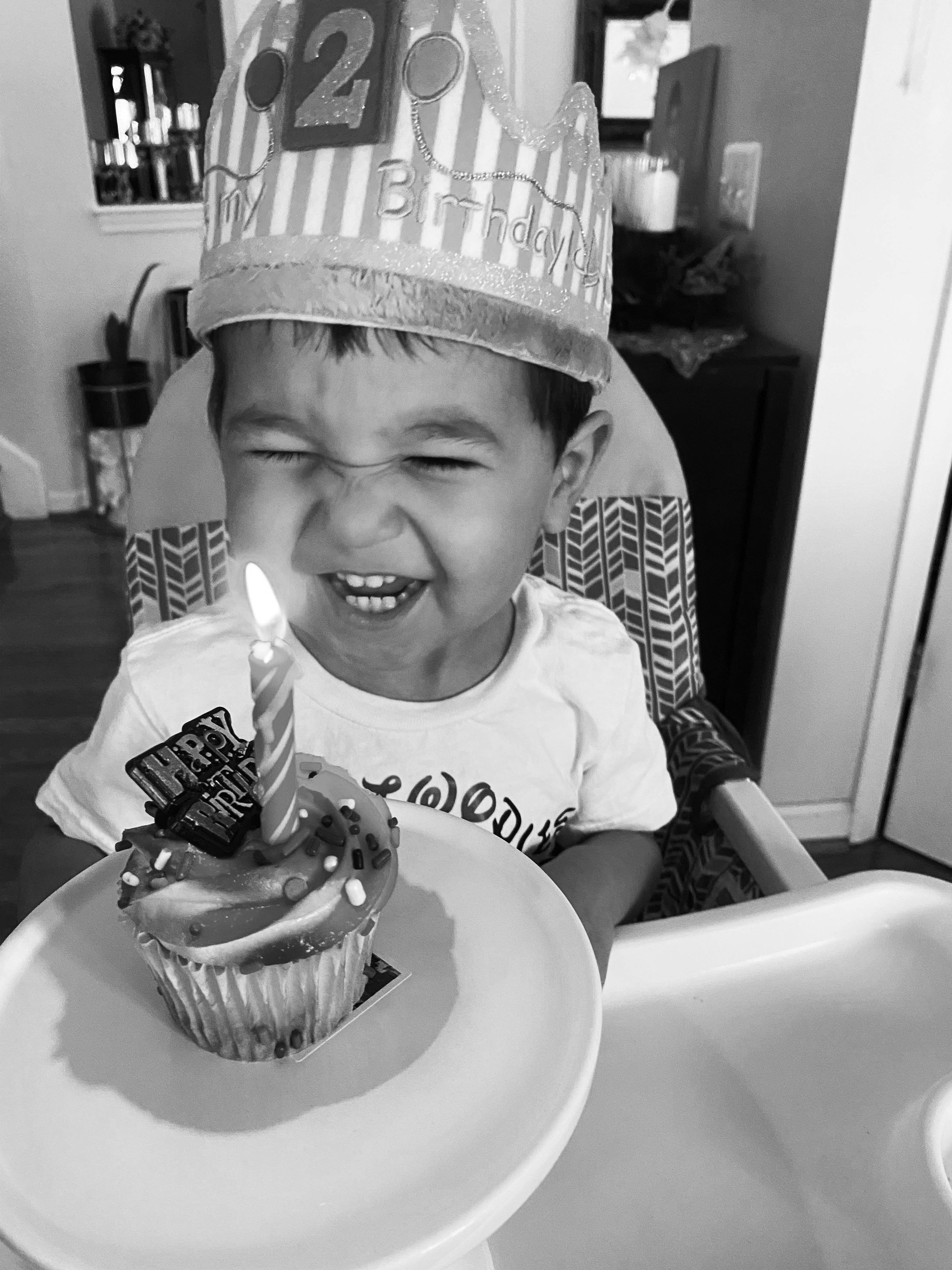 Child wearing a birthday crown blowing out a candle on a cupcake