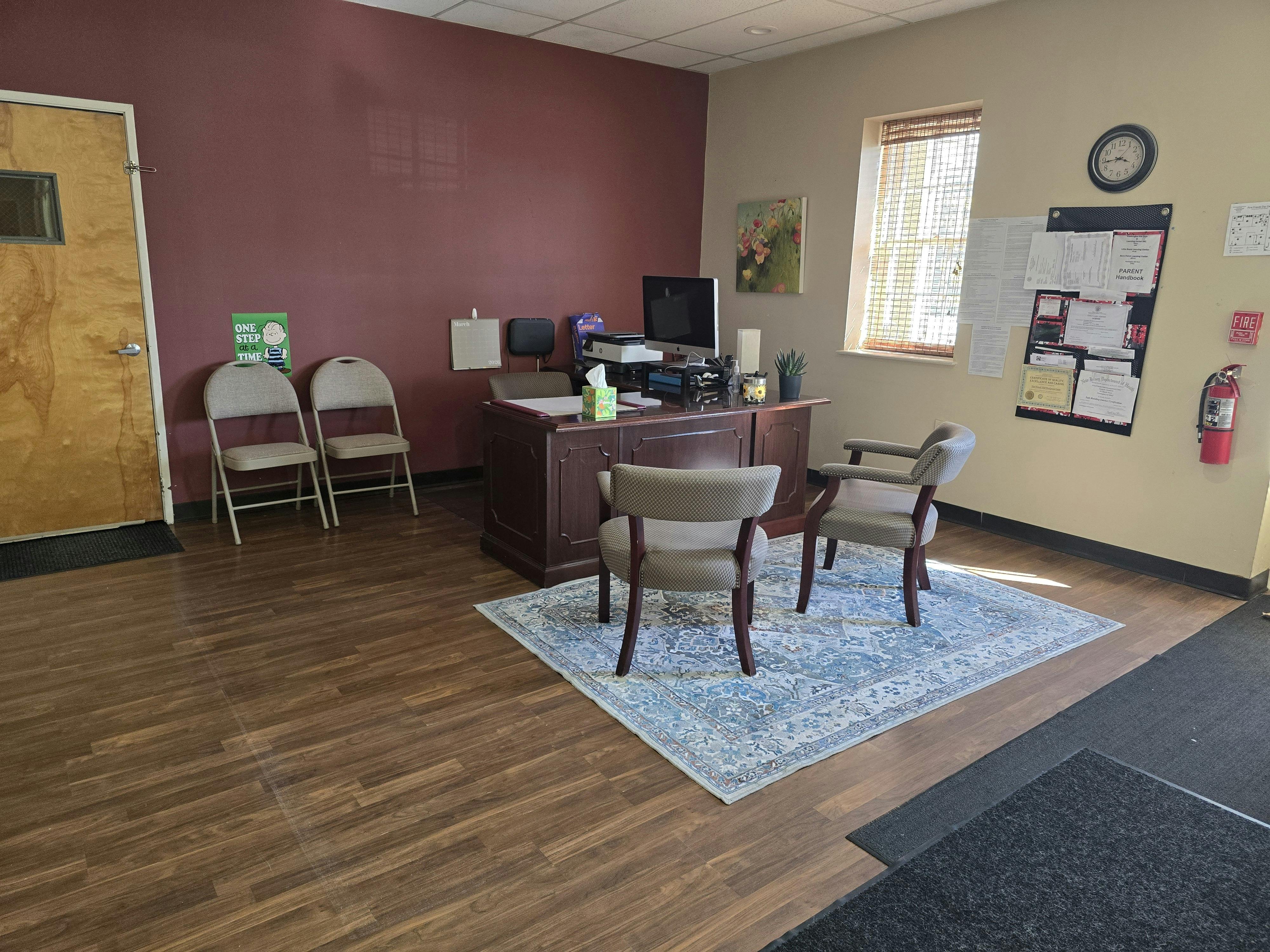 Reception area with a wooden desk, two chairs, and a 'One Step at a Time' sign