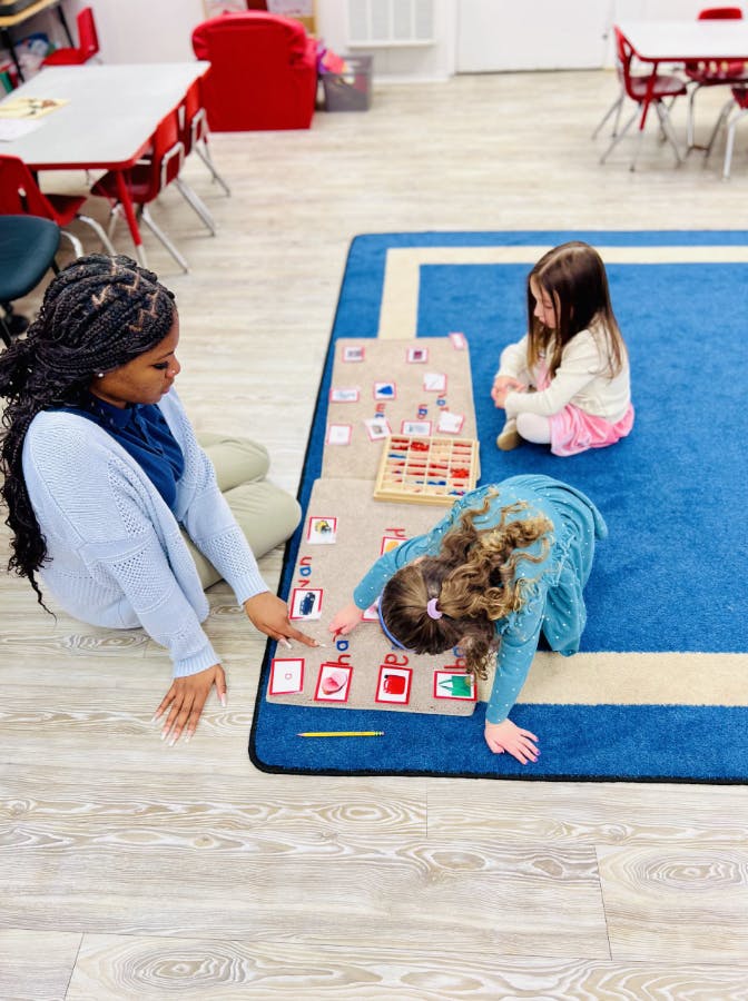 Teacher and child working on alphabet cards on a blue rug in a classroom