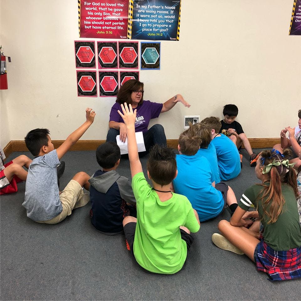 Adult teaching children sitting on the floor, some children raising hands