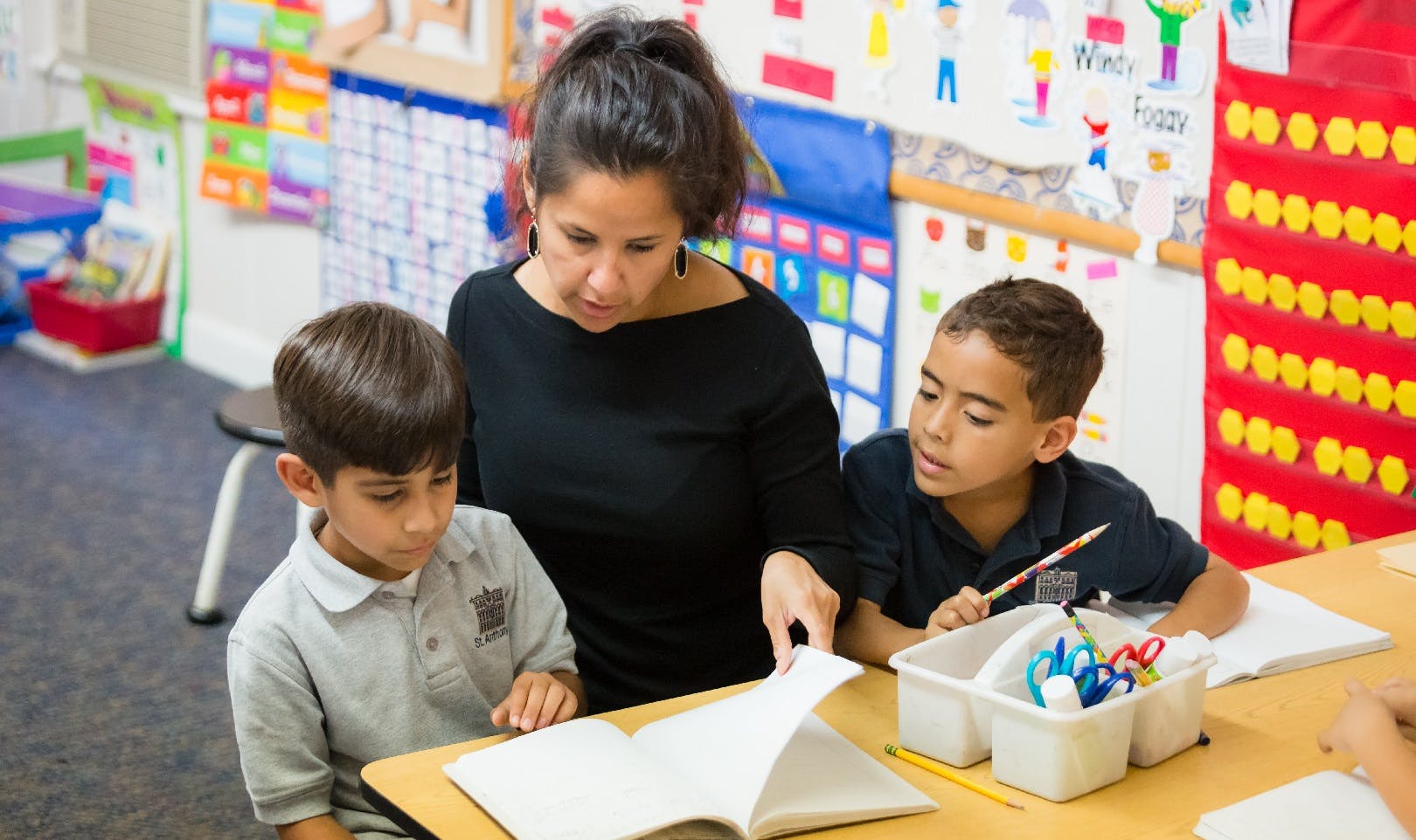 Person helping two children read a book in a classroom