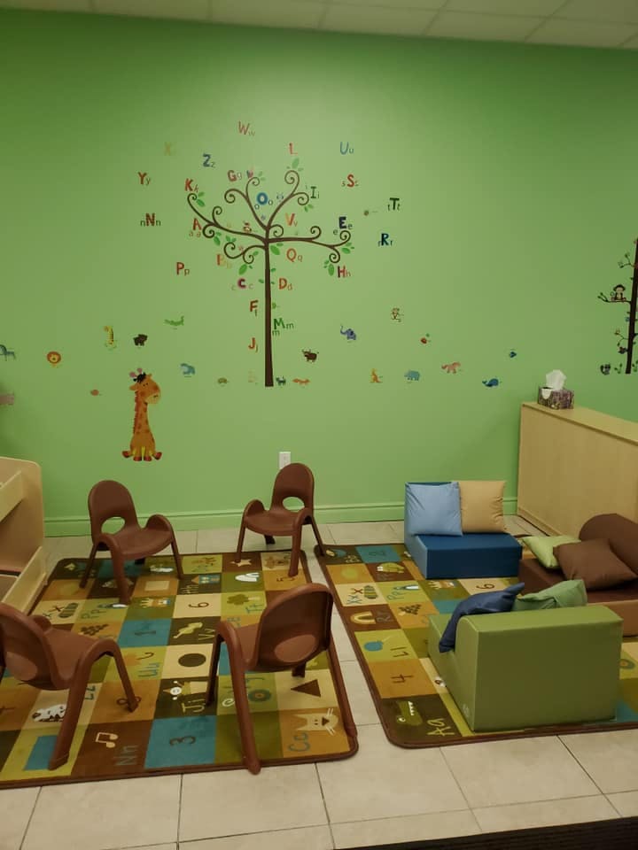 Classroom with green walls, alphabet tree decal, small chairs, and play mats