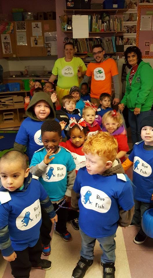Adults and children in a classroom, some children wearing blue shirts with "Blue Fish"