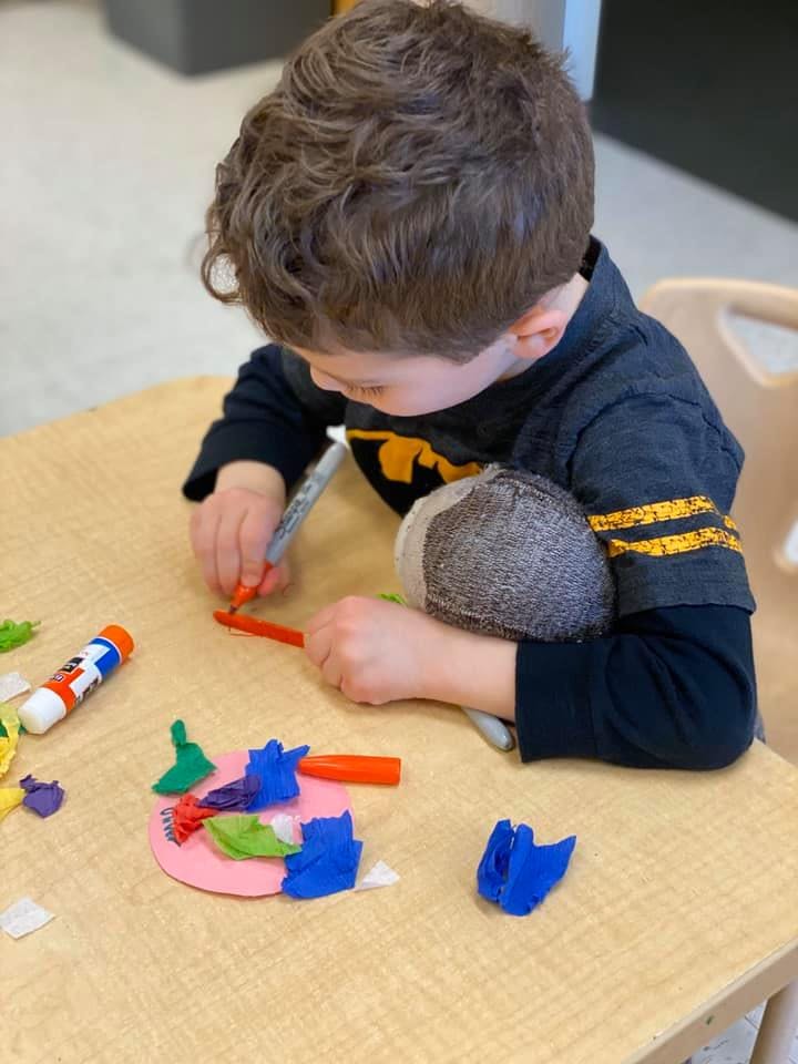 Child creating art with colorful paper and glue stick on a table
