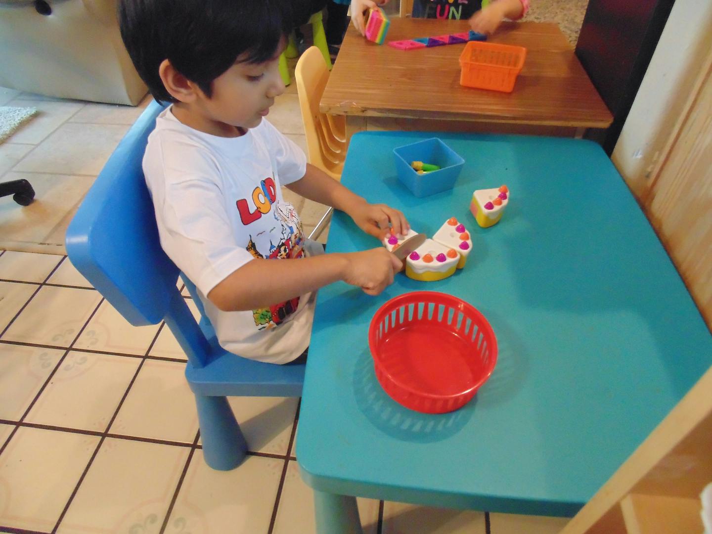 Child cutting a toy cake with a toy knife at a table