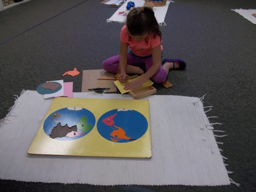 Child working on a world map puzzle in a classroom