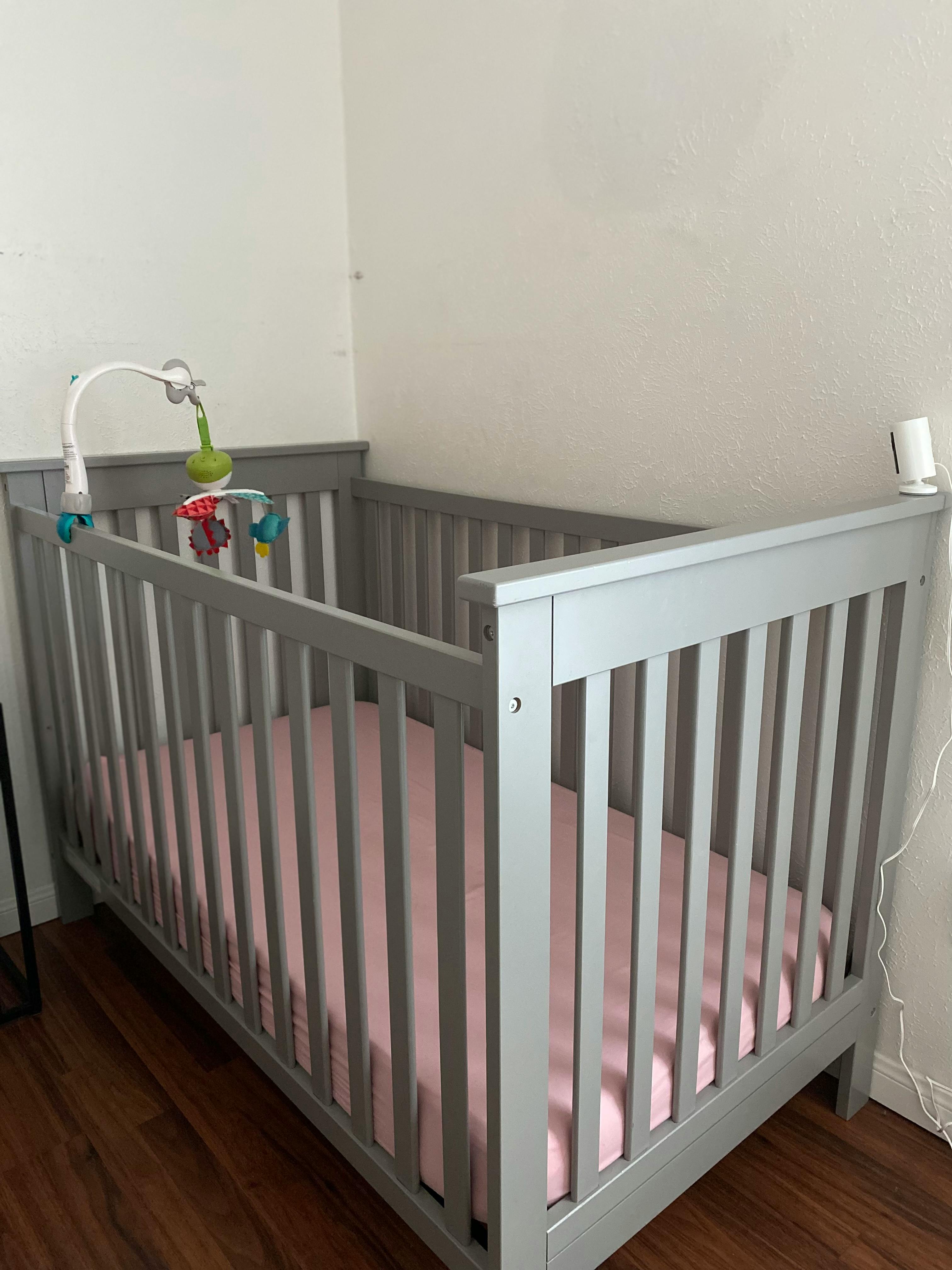 Gray crib with a pink sheet and a baby mobile attached