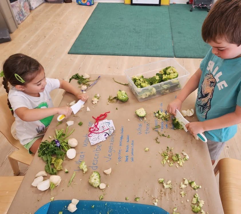 Two children cutting vegetables at a table