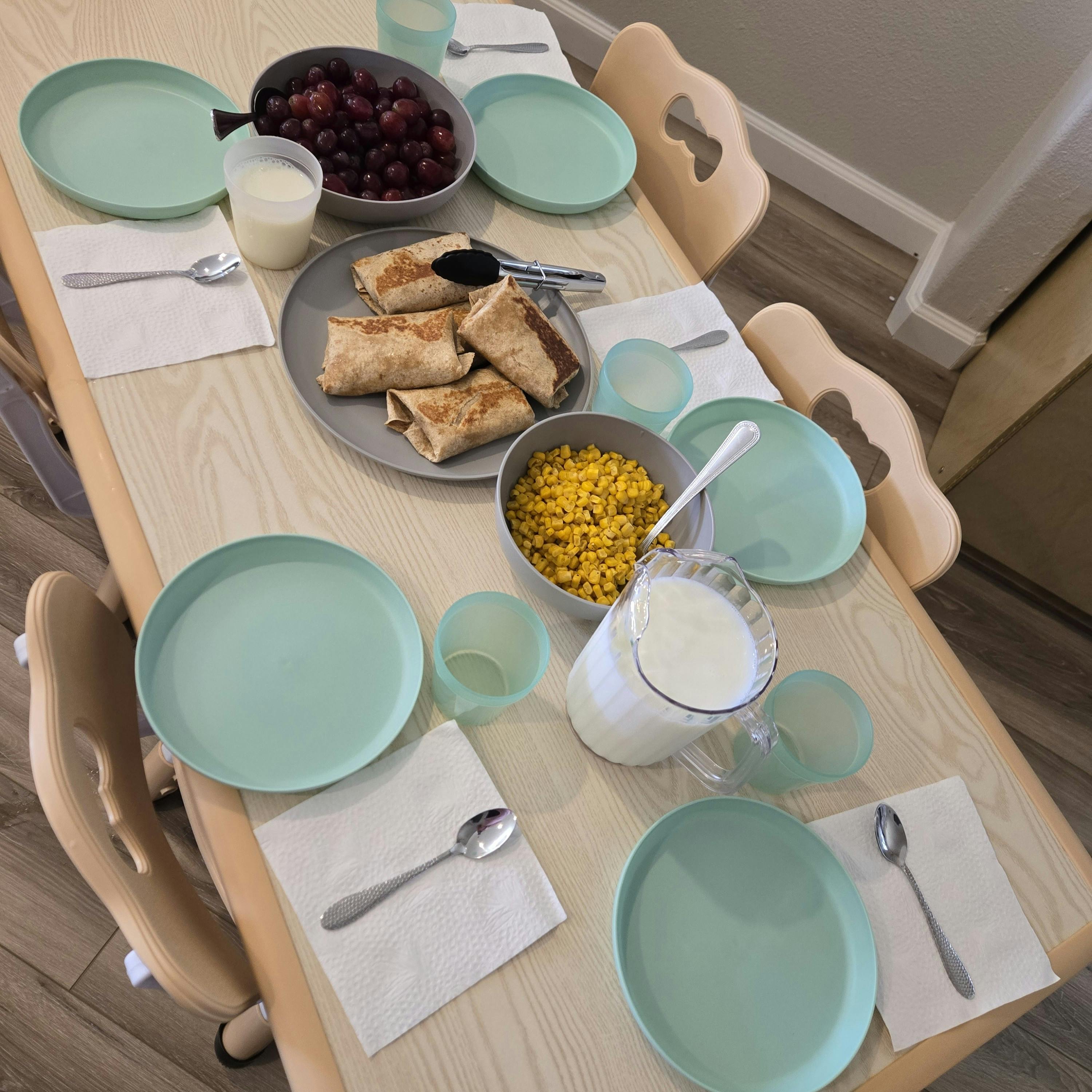 Table set with plates, silverware, burritos, corn, and cherries
