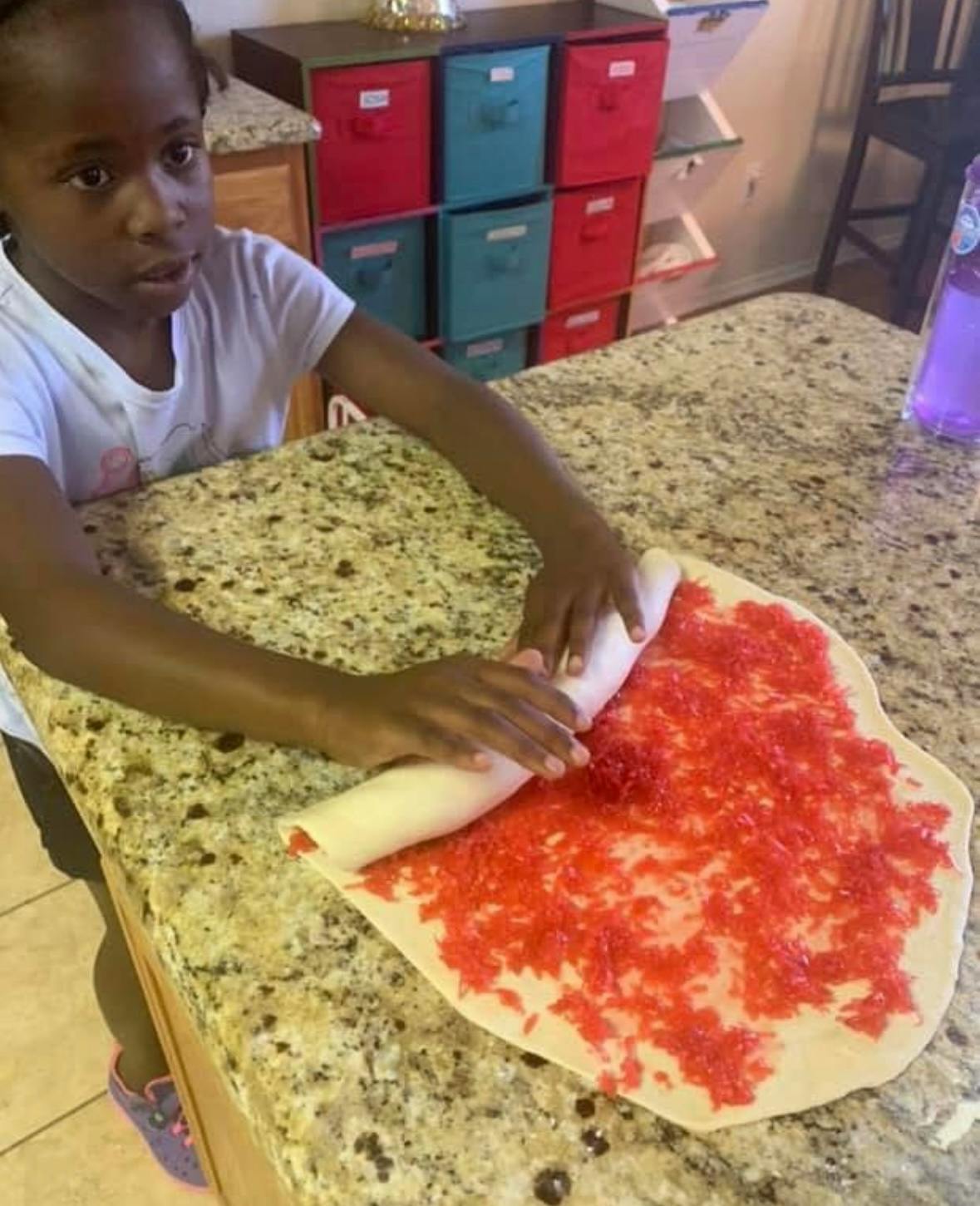 Child rolling dough with red sprinkles on a kitchen counter