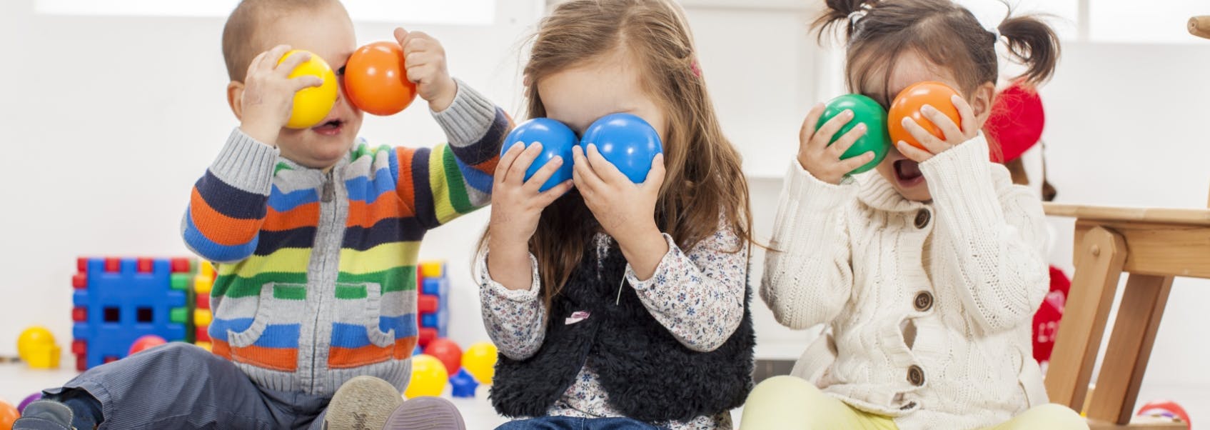 Three children holding colorful balls over their eyes