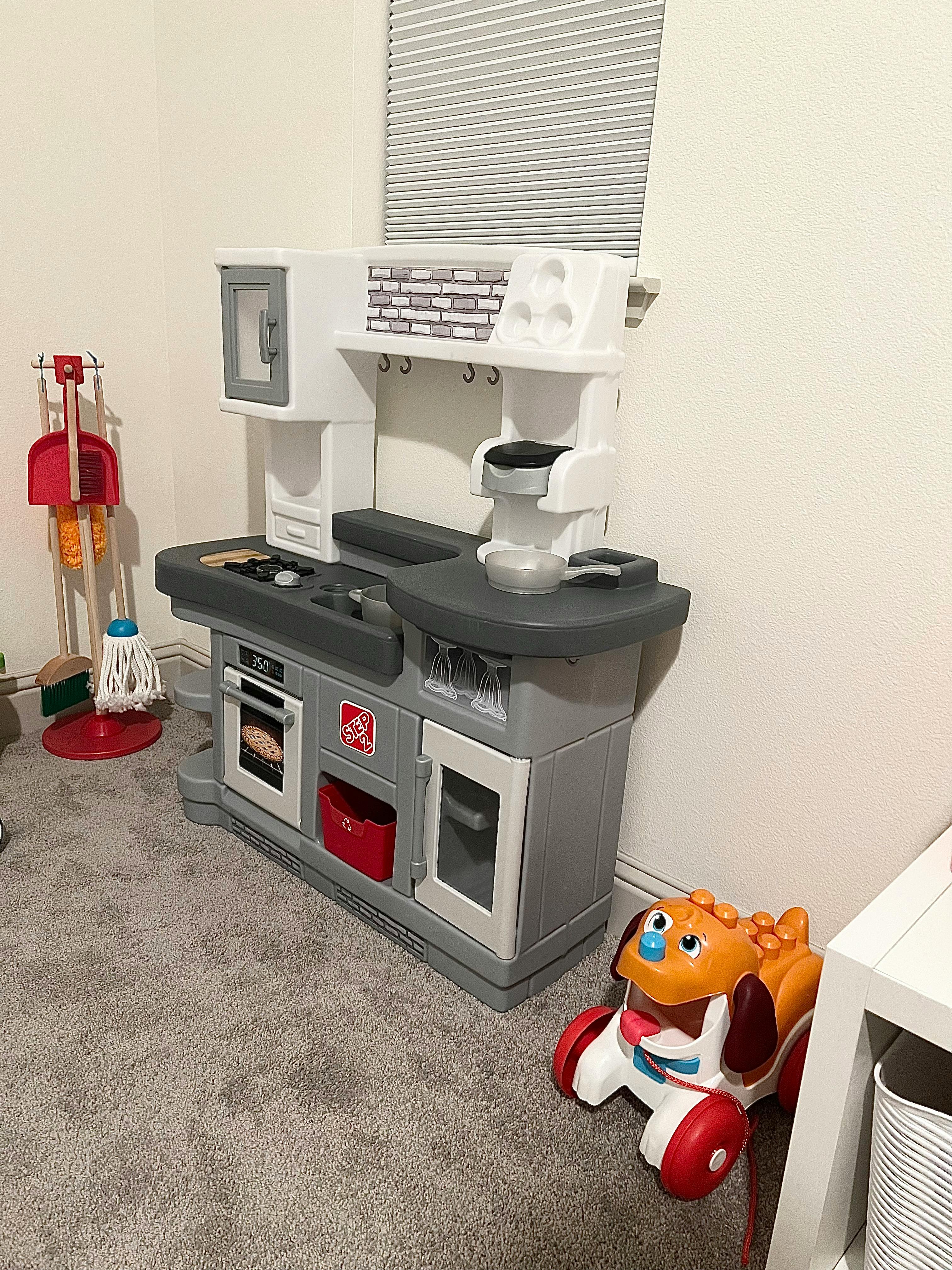 Child's play kitchen with a toy cleaning set and ride-on toy nearby
