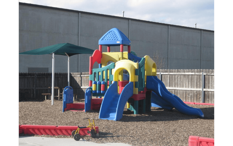 Colorful playground structure with slides and a green shade canopy over wood chips
