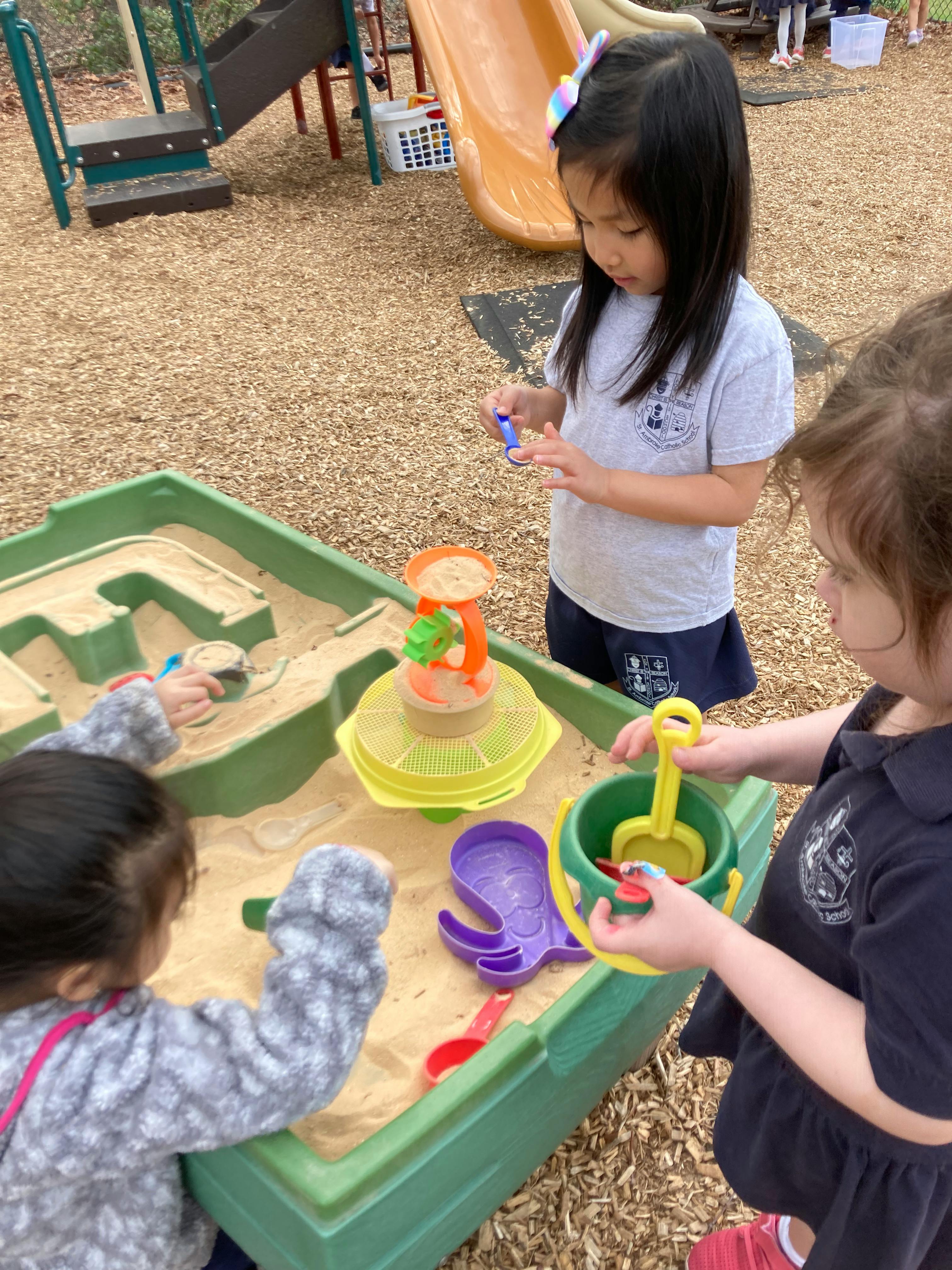 Three children playing in a sandbox with toys