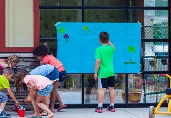 Children painting on a large blue sheet outdoors