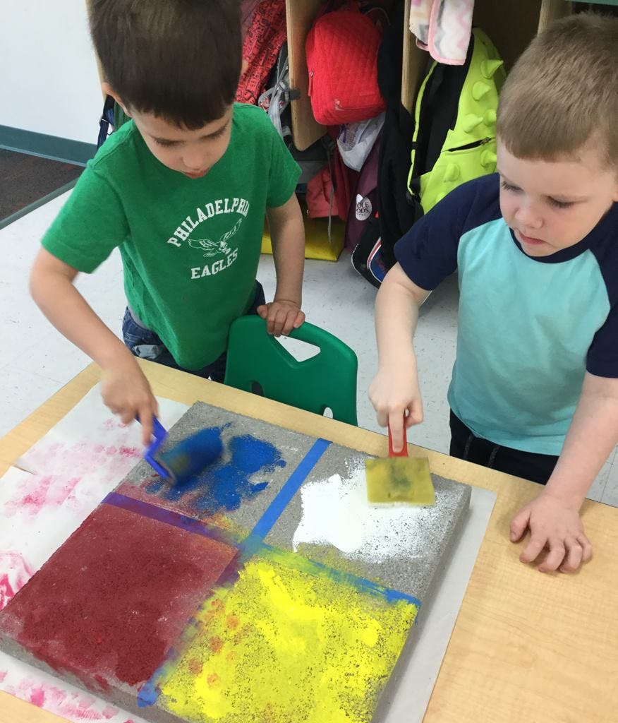 Two children painting on a surface with multiple colors