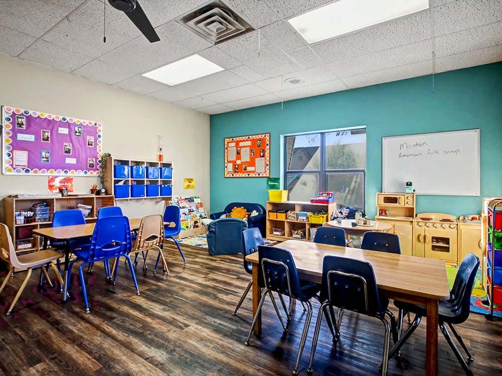 Children's classroom with tables, chairs, shelving, and play kitchen area