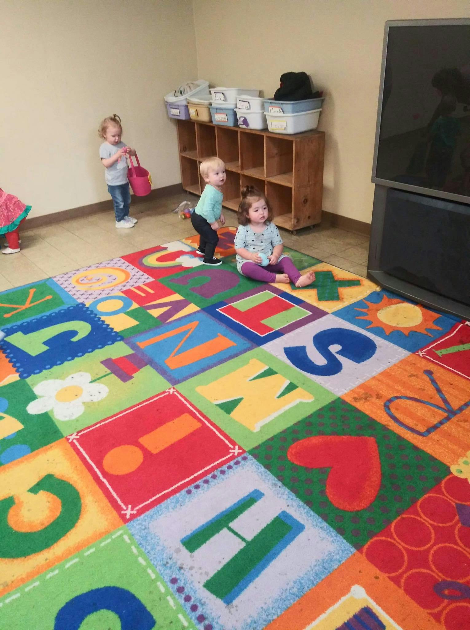 Three children playing on a colorful alphabet rug in a room