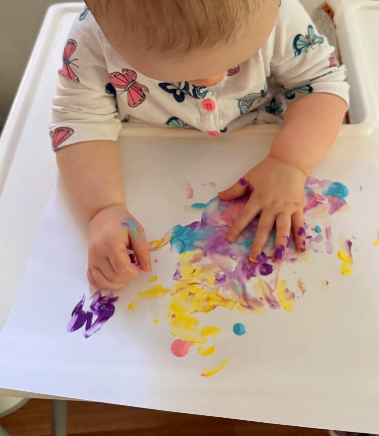 Child finger painting on paper in a high chair