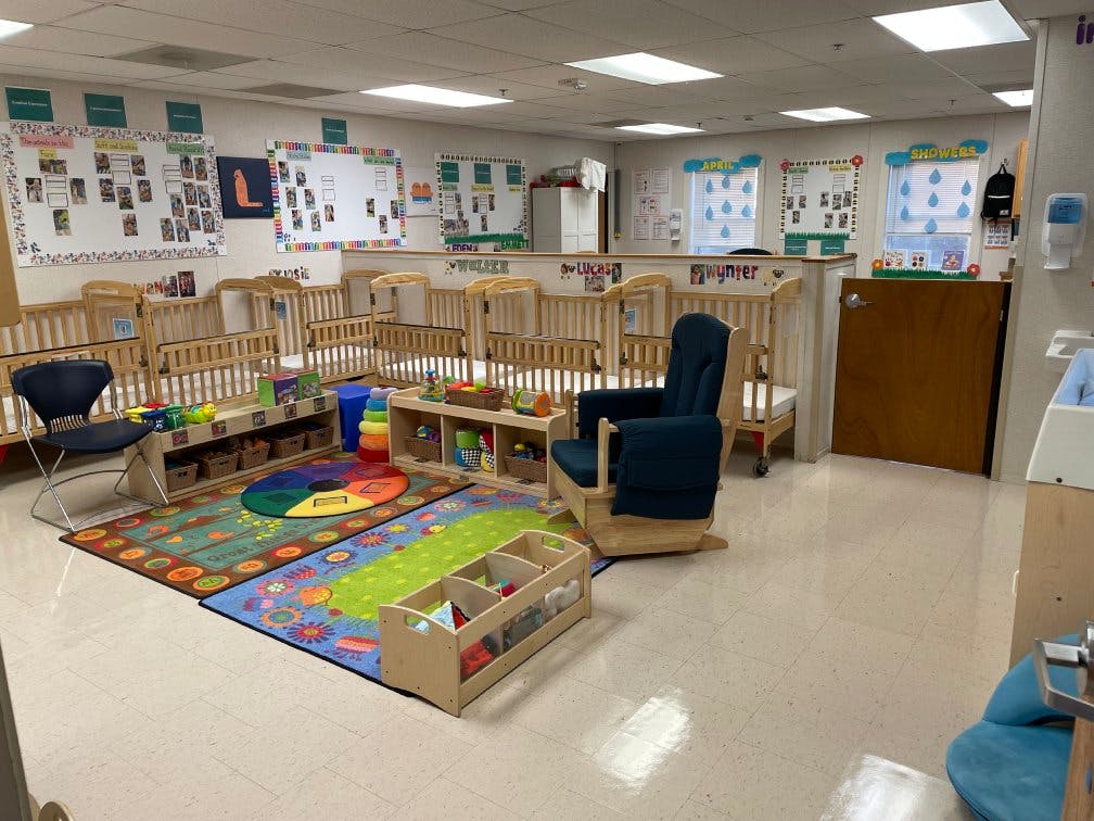 A room with several cribs, a rocking chair, rugs, and shelves with toys
