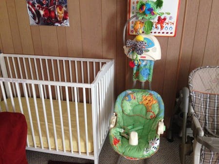 White crib with yellow sheet next to a green baby bouncer